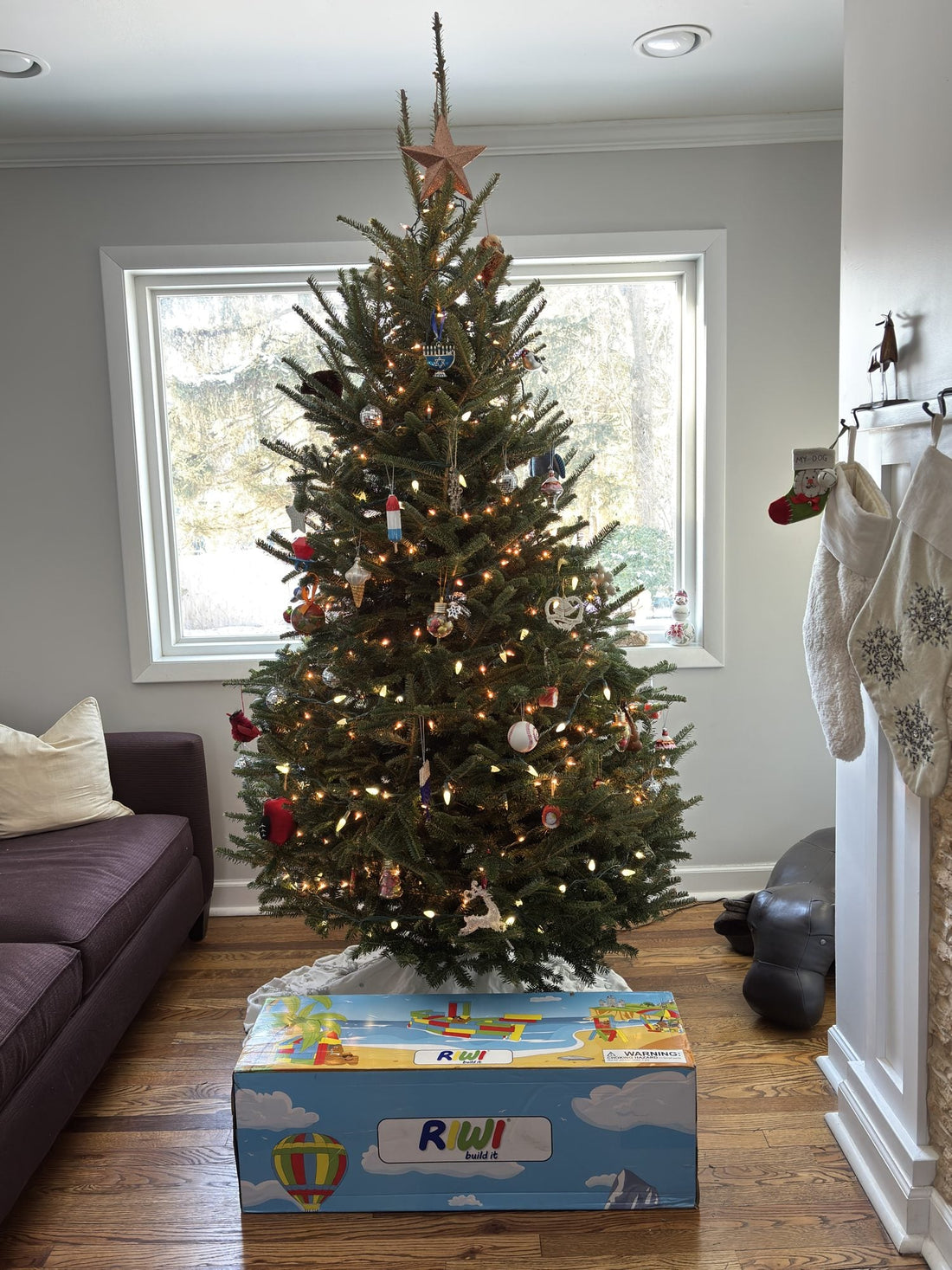 Ungeöffneter RIWI® Karton mit XXL-Bausteinen als Weihnachtsgeschenk unter einem geschmückten Weihnachtsbaum im Wohnzimmer
